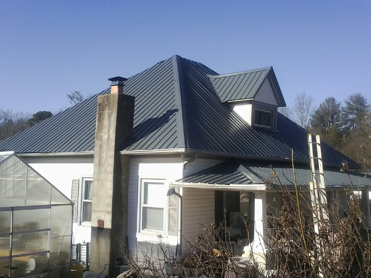 Dark blue standing seam metal roof on a white farmhouse with dormer — Slate & Tile Roof Repair by Roofing Brothers in Cowen