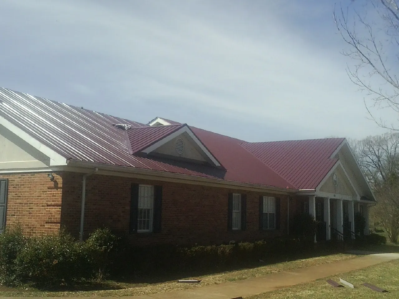 Red metal roof with gabled entries on a long brick building, from a Hail Damage Roof Repair job in Cowen