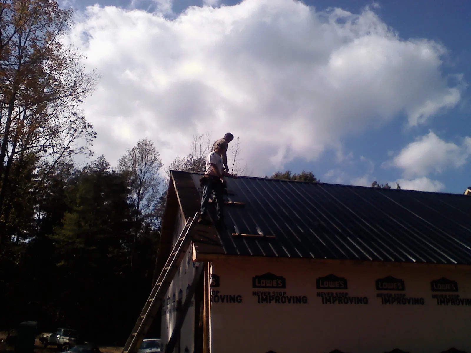 Roofer fastening dark metal panels high against a cloudy sky, from a Roof Inspection job in Cowen