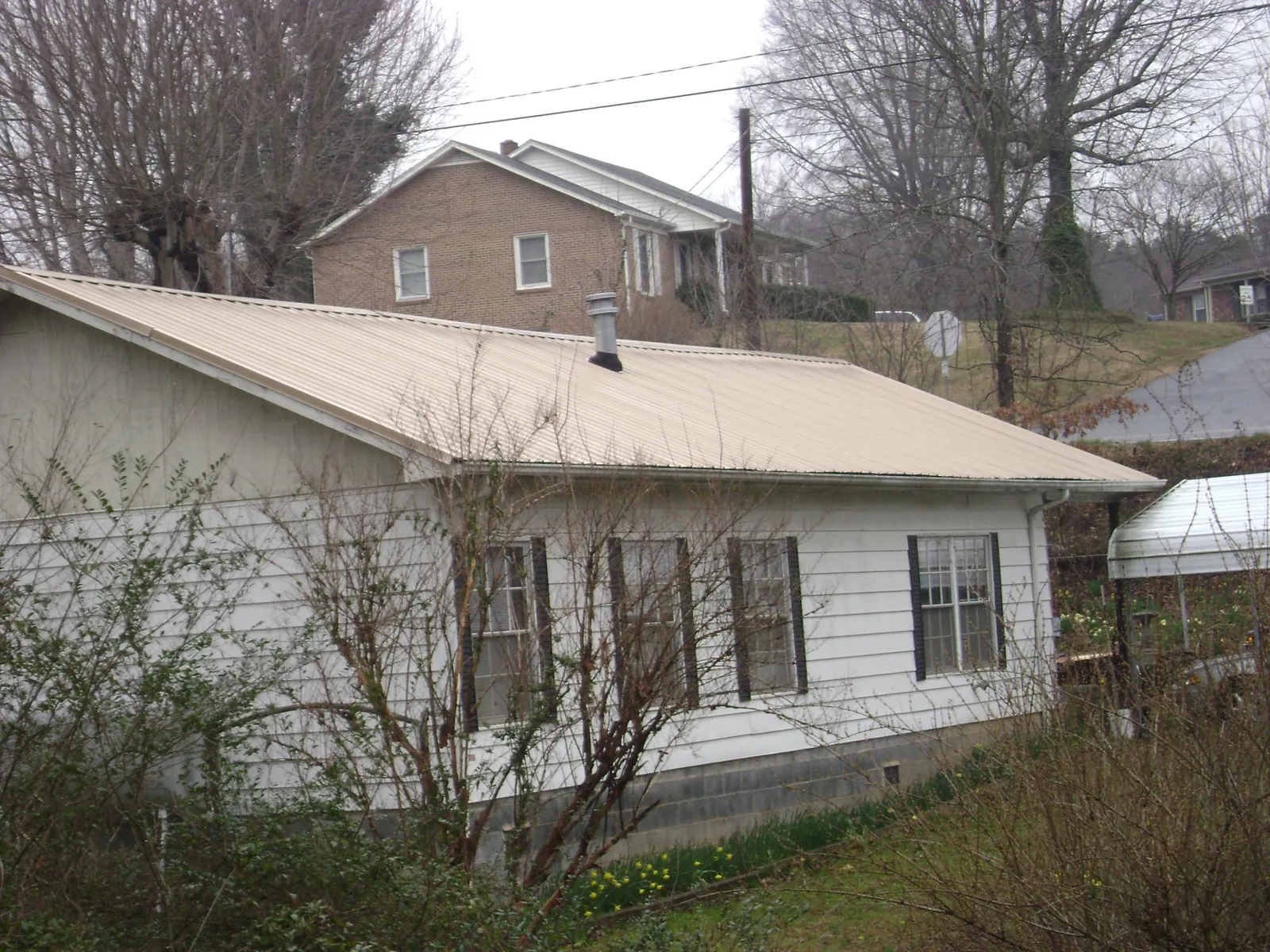 Tan metal roof on a white sided house set into a hillside — Commercial Roofing by Roofing Brothers in Cowen
