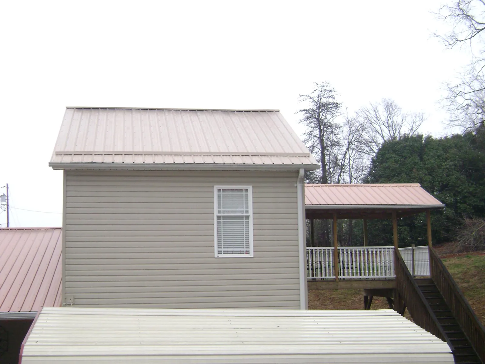 Tan metal roofs on a two story addition and attached porch, from a Roof Replacement job in Cowen